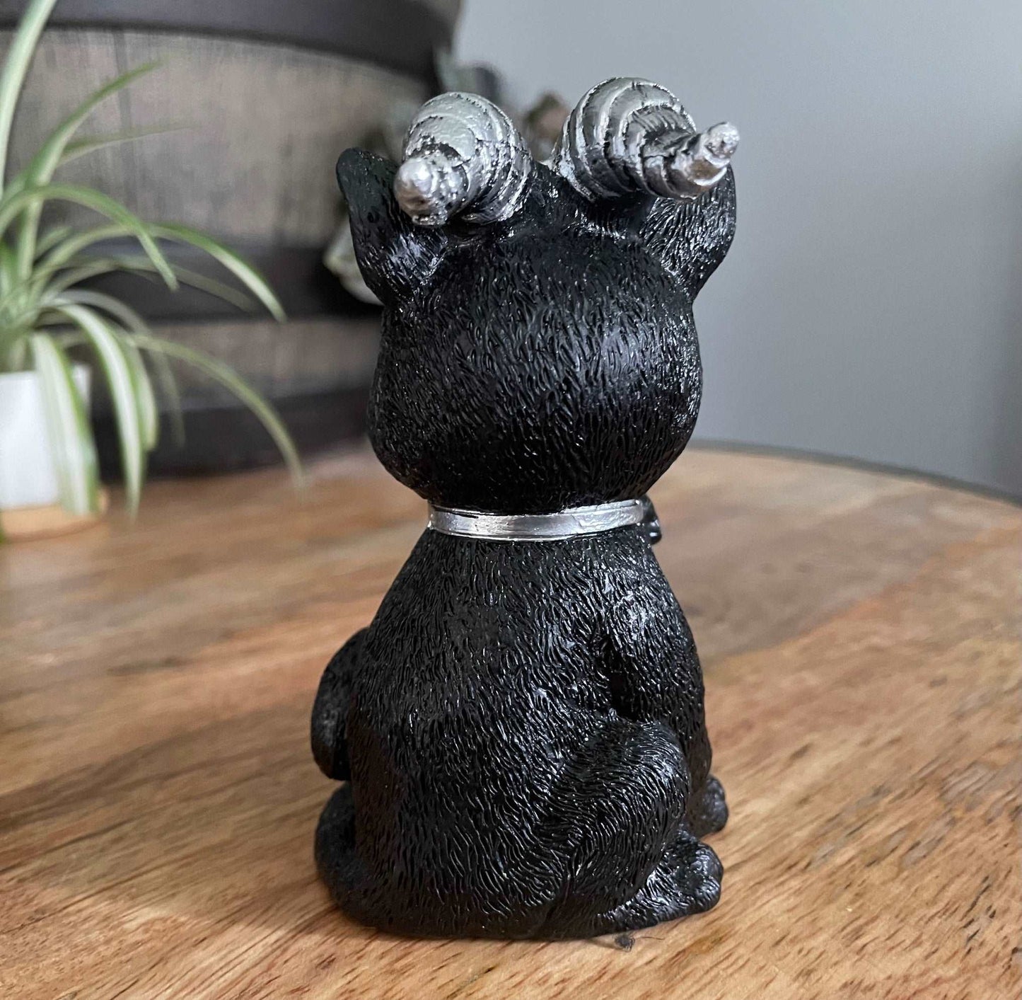 Pictured is a resin statue of a black cat with horns and a pentagram on its forehead with a paw on a silver skull. Demon Cat Figurine back