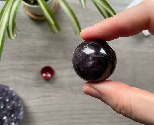 A polished sphere of amethyst is shown in the image. The crystal is a purple color and has a smooth, shiny surface. Amethyst Crystal Sphere 31mm (B)