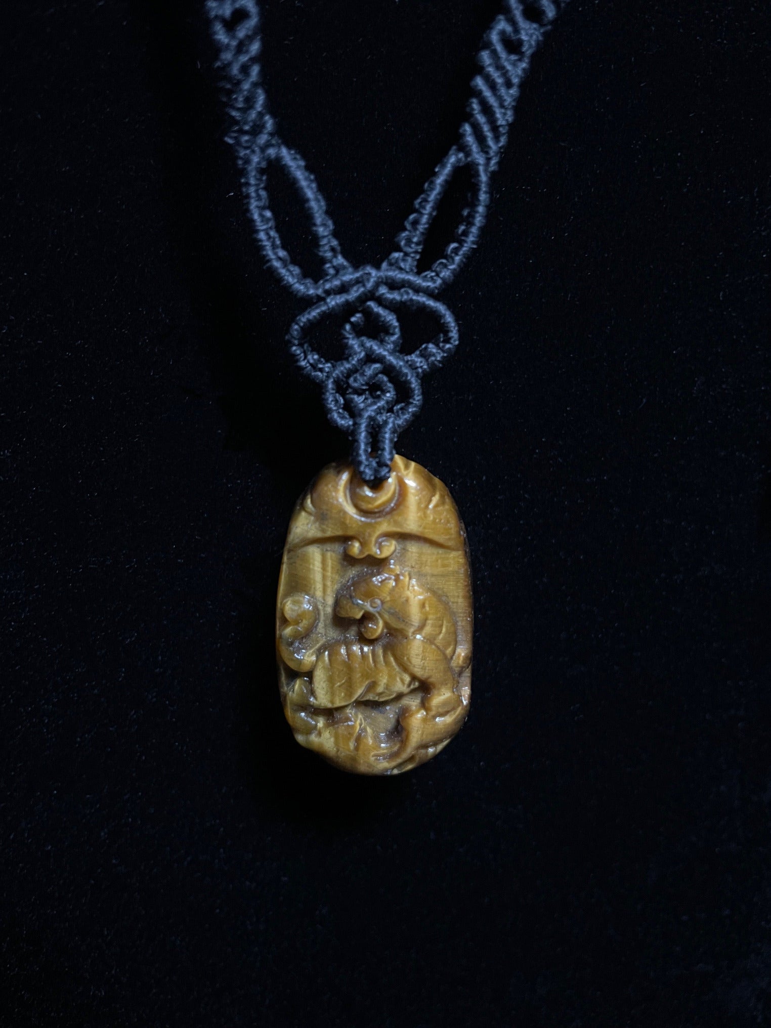 A picture of a tiger pendant carved out of tiger's eye stone. The pendant is on an intricate black macrame necklace. Tiger's Eye Tiger Macramé Necklace (Twisted Nightshade Jewellery) - The Wandering Fox Emporium, Your Crystal Store black