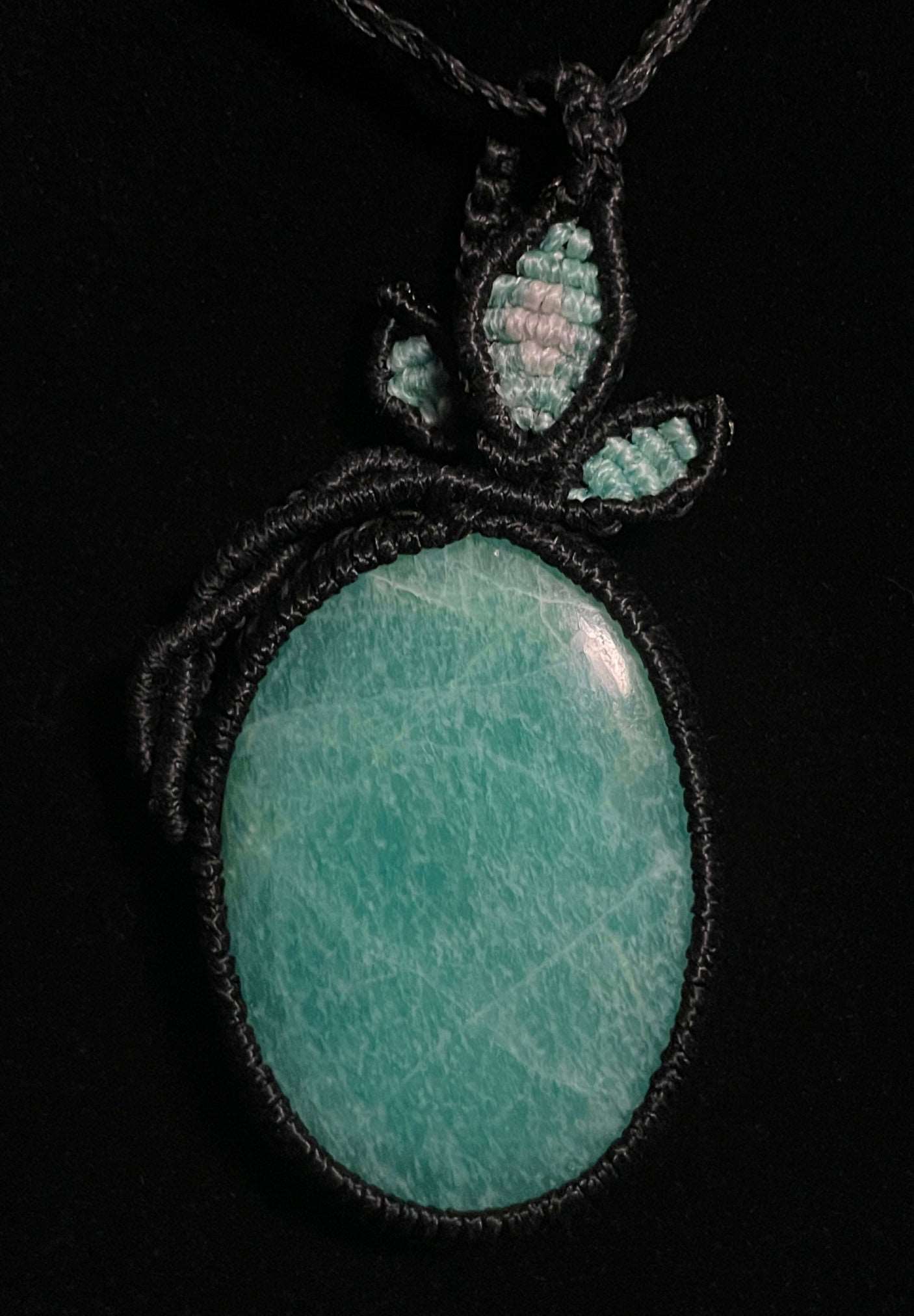 Pictured is an amazonite cabochon wrapped in macrame thread. A gothic book and flowers are nearby. Amazonite Macramé Necklace (Twisted Nightshade Jewellery) - The Wandering Fox Emporium, Your Crystal Store black