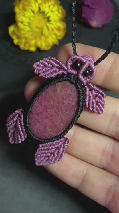 Pictured is a rhodonite cabochon wrapped in macrame thread. The rhodonite pendant is in the shape of a sea turtle. A gothic book and flowers are nearby. Rhodonite Sea Turtle Macramé Necklace (Twisted Nightshade Jewellery) Strawberry Quartz Pink Macramé Necklace (Twisted Nightshade Jewellery) - The Wandering Fox Emporium, Your Crystal Store video