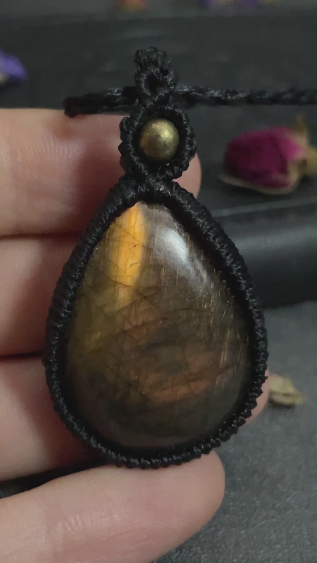 Pictured is a labradorite cabochon wrapped in macrame thread. A gothic book and flowers are nearby. Sunset Labradorite Teardrop Macramé Necklace (Twisted Nightshade Jewellery) - The Wandering Fox Emporium, Your Crystal Store video